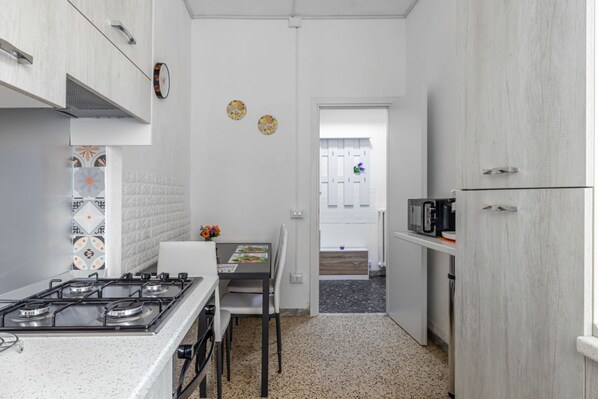 Una cucina compatta con piano cottura a gas, mobili bianchi, un tavolo con sedie e un forno a microonde.