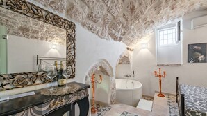 A bathroom with a stone ceiling, a bathtub, a sink, and a mirror with a decorative frame. - Donna Alfa Suite by Rentbeat (Ostuni)