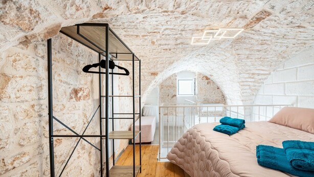 Ein Schlafzimmer mit Steinwand, einem Bett mit blauen Handtüchern, einer Holzleiter und einem weißen Geländer.