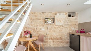 Eine Küche mit Steinwand, einem Holzespeisetisch mit Stühlen, einer kleinen Kühlbox und einer Treppe.