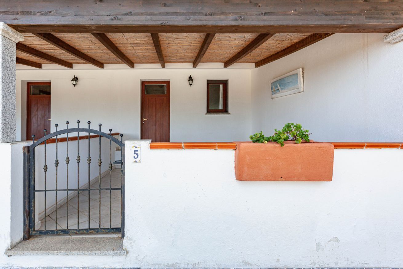 Um edifício com fachada branca, teto de madeira, portão de metal e um vaso com plantas verdes.