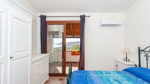 A bedroom with a bed, a dresser, a nightstand, an air conditioner, and a balcony with a view. - Comino Alto - Appartamento 5 by Rentbeat (Siniscola)