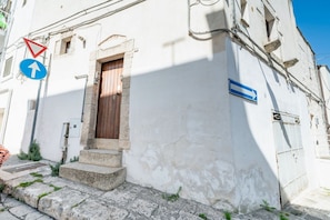 Um edifício com porta de madeira, degraus de pedra e uma placa indicadora azul.