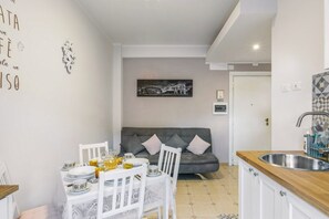 A compact kitchen with a dining area, a grey sofa, and a wall-mounted picture.