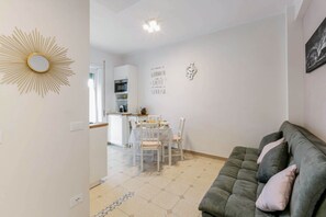 A modern living room with a sofa, a dining area with a table and chairs, and a kitchen in the background.