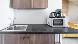 Eine kompakte Küche mit Spüle, einem schwarzen Induktionskochfeld, einer weißen Mikrowelle und einer Kaffeemaschine.