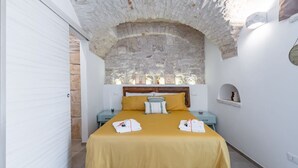 Ein Schlafzimmer mit Steingewölbe, einem Bett mit gelber Bettwäsche, zwei Nachttischen und einem kleinen Regal.