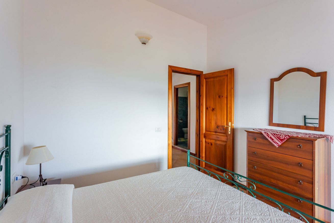A bedroom with a bed, dresser, mirror, and a door leading to another room.