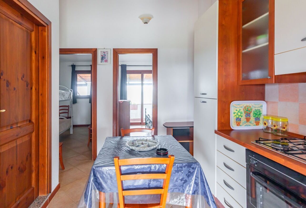 Una cocina con una mesa cubierta de plástico, armarios de madera y una estufa.