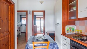 A kitchen with a table covered in plastic, wooden cabinets, and a stove. - Comino Alto - Appartamento 6 by Rentbeat (Siniscola)
