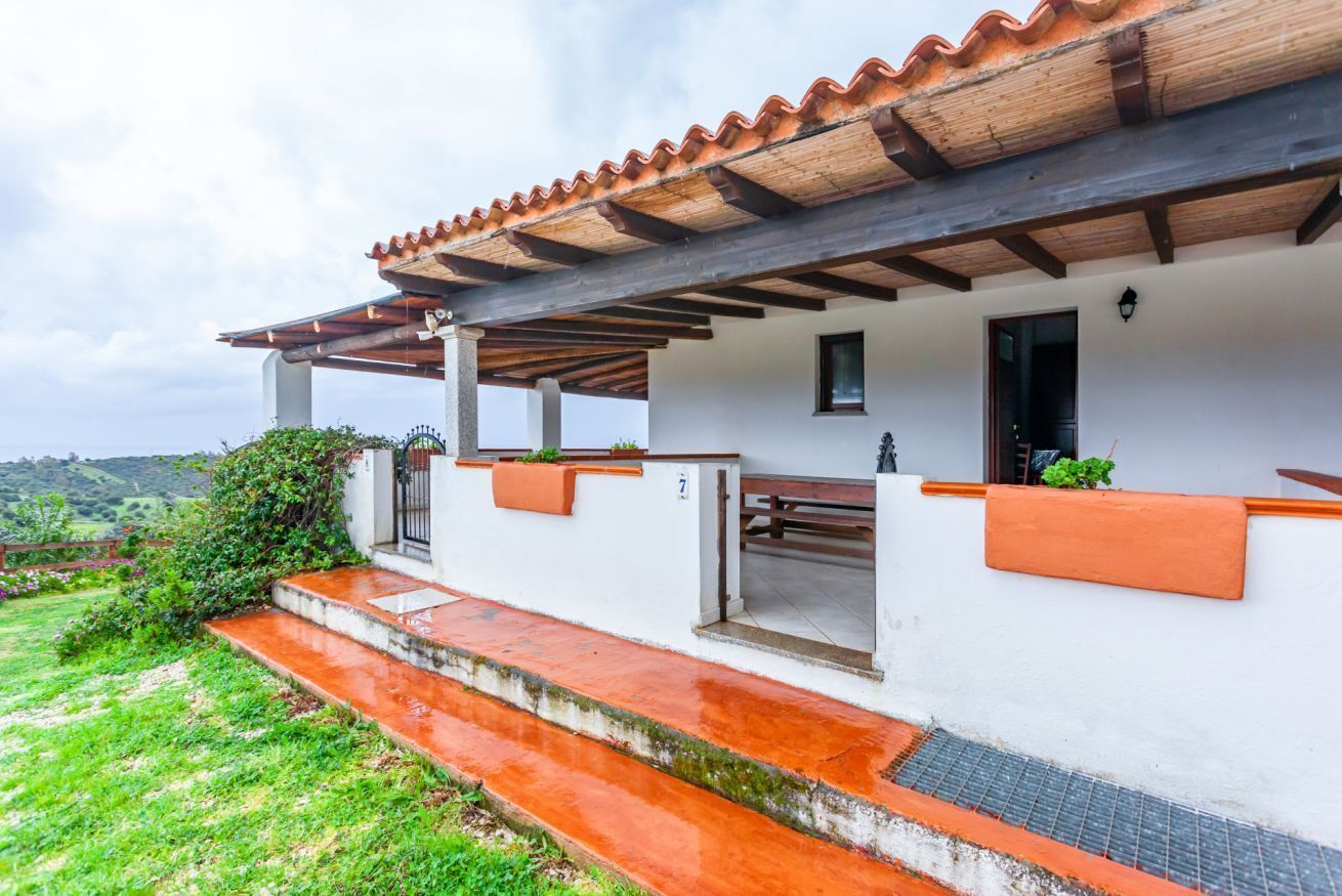 Un bâtiment blanc avec un toit en tuiles, un porche abrité et un petit jardin.