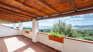Eine überdachte Terrasse mit Blick auf die Landschaft, mit Holzbalkendecke und Terrakottafliesen.
