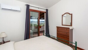 Ein Schlafzimmer mit Bett, Kommode, Spiegel und einer Schiebetür zum Balkon mit Blick.