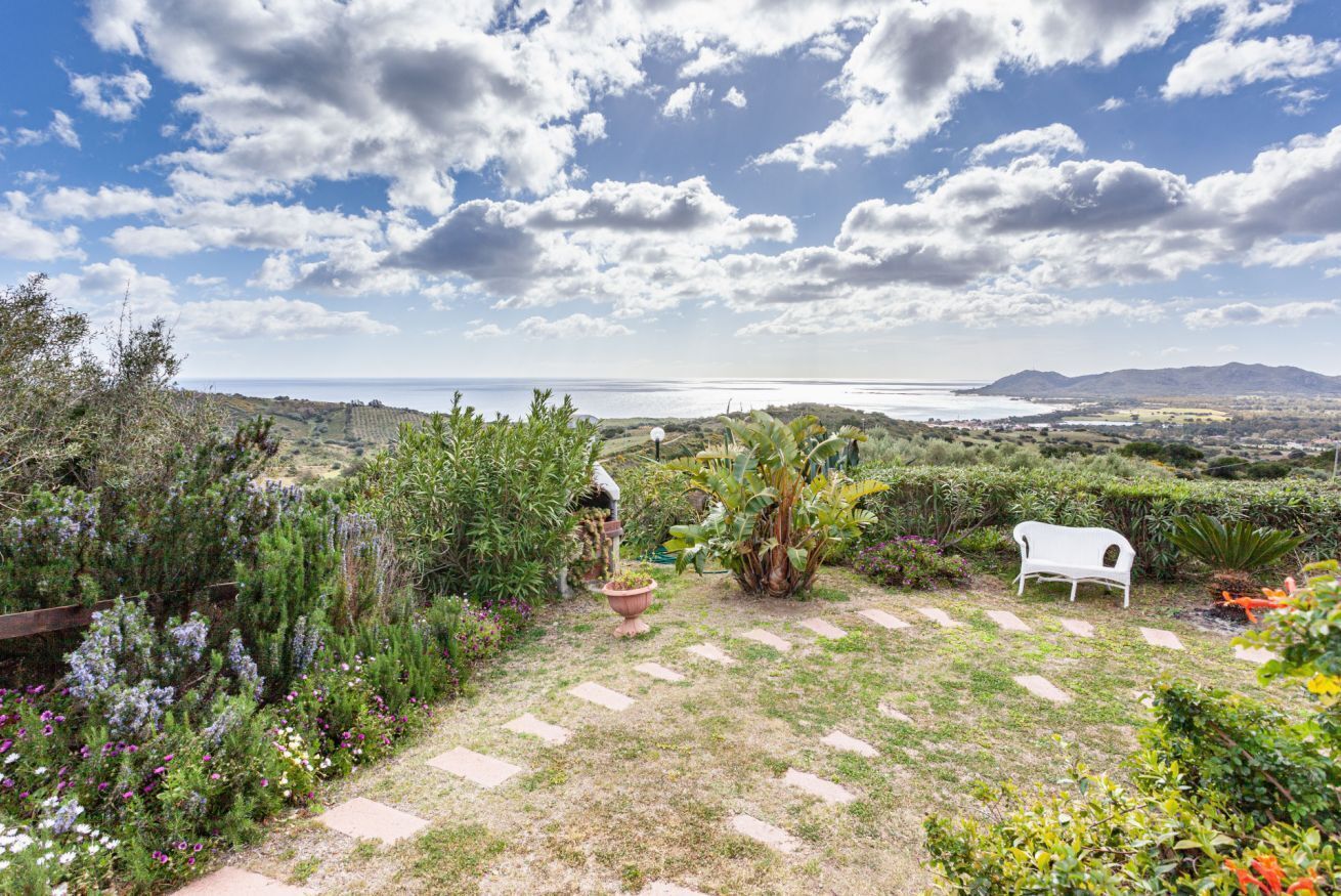 Ein Garten mit einer weißen Bank, einem Weg und Blick auf das Meer und die Berge.