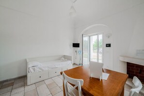 Een kamer met een houten tafel, witte stoelen, een witte bank, een televisie en een open haard.