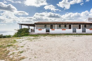 Un bâtiment situé sur la côte, doté d’une façade blanche, d’un toit recouvert de tuiles rouges et d’une allée gravillonnée.