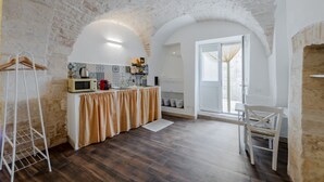 A kitchen with a rustic stone ceiling, a wooden floor, and a white countertop with a microwave and other appliances.