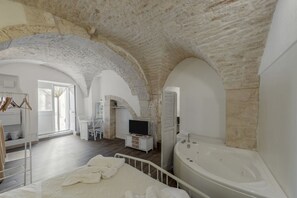 A spacious bedroom with a large bed, a sitting area with a TV, and a bathroom with a bathtub. - Suite Violetta by Rentbeat (Martina Franca)