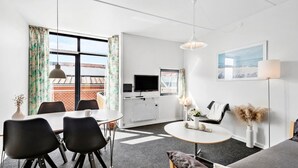 A modern living room with a dining area, a flat-screen TV, and a large window with curtains. - 1 bedroom gorgeous apartment in Fanø (Fanø)