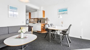 A modern, compact living space with a kitchenette, a dining area with a round table and chairs, and a grey sofa. - 1 bedroom gorgeous apartment in Fanø (Fanø)