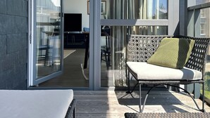 Ein moderner Balkon mit Glastür zu einem Innenbereich, Korbmöbeln und Blick ins Freie.