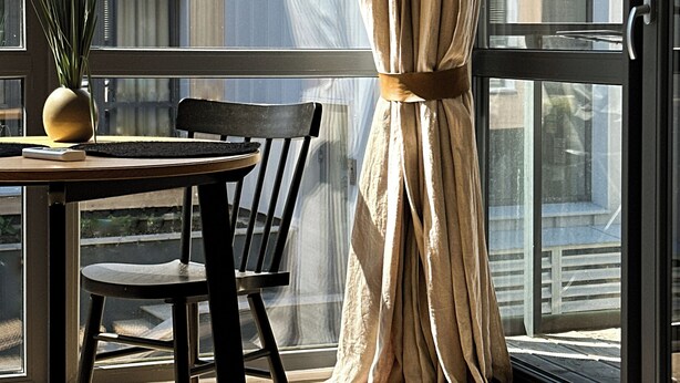 A modern room with a dining table, chairs, a potted plant, and a large window with curtains.