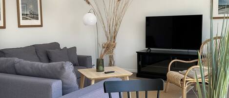 A modern living room with a grey sofa, a wooden coffee table, a black TV stand, and a wicker chair.