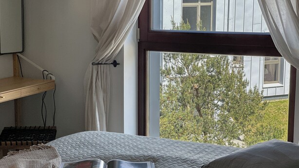 Un dormitorio con una cama, un libro, un escritorio y una ventana con vistas a árboles.