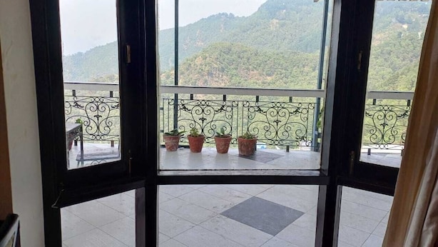Une chambre avec vue sur un balcon agrémenté de plantes en pot et sur un paysage montagneux.
