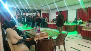 Une salle de conférence avec des tables et des chaises, une banderole avec du texte, et des personnes debout et assises.