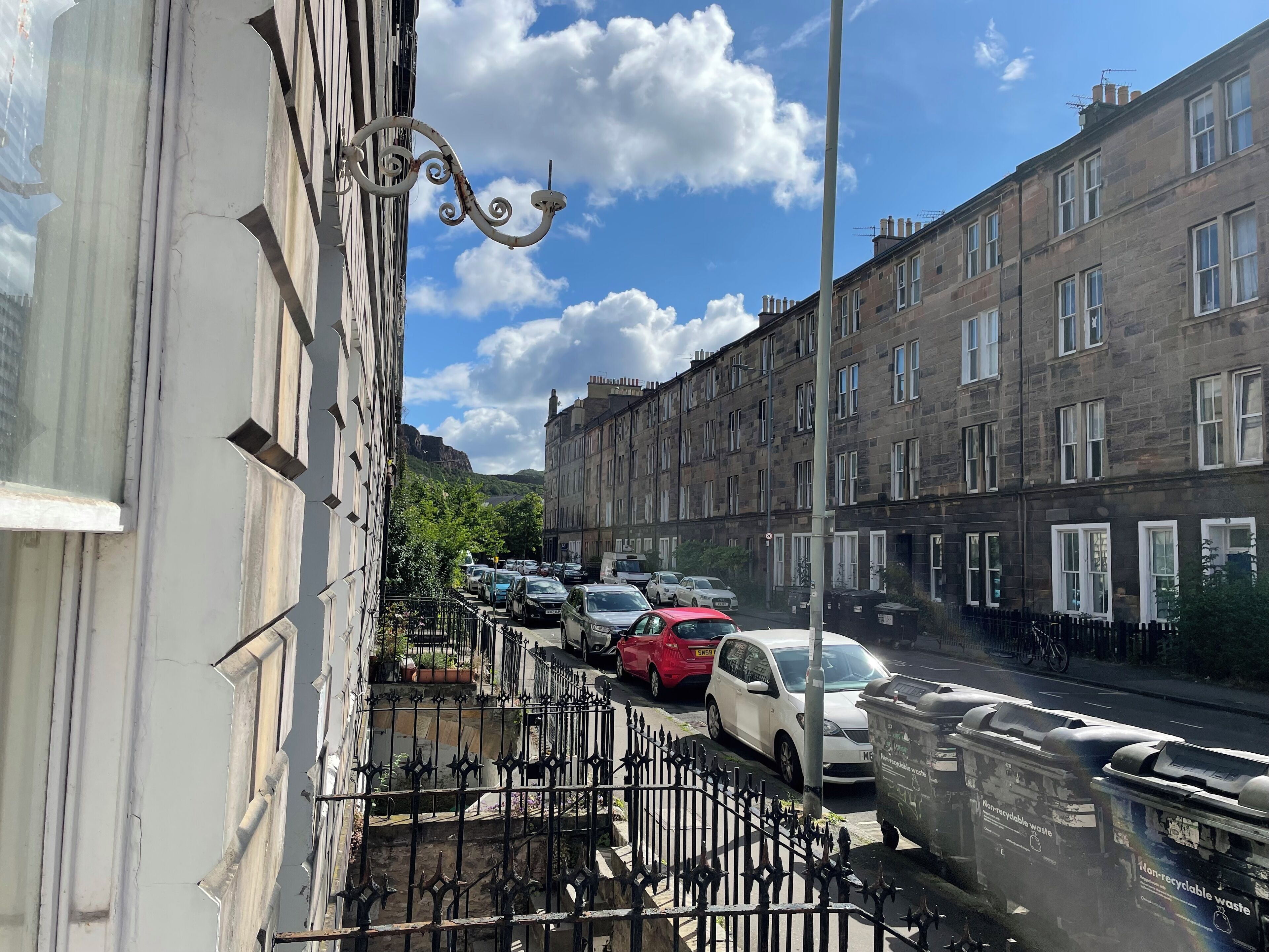 A street view with parked cars, a row of terraced houses, and a clear sky.
