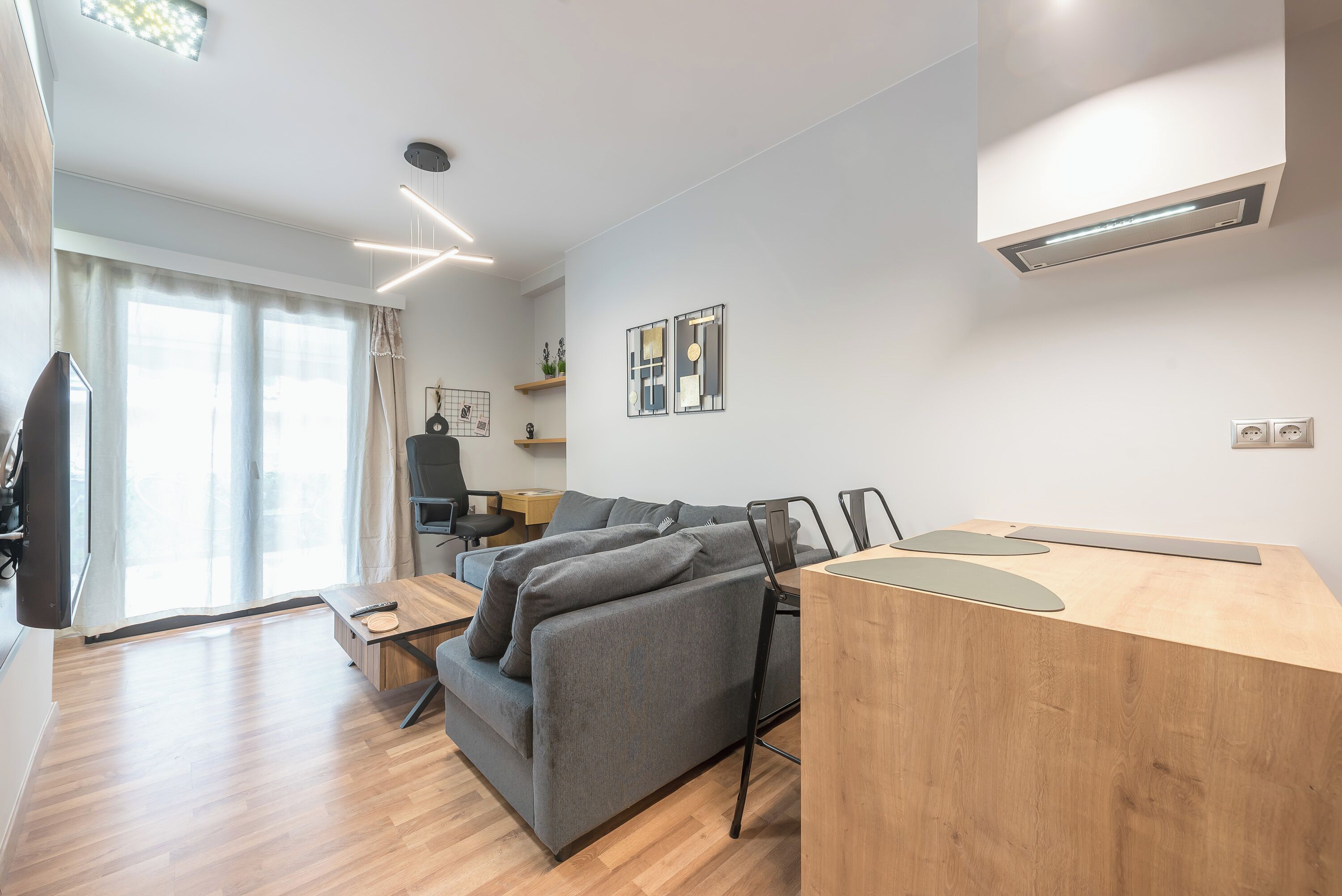 Een moderne woonkamer met een grijze bank, een houten eettafel en een flatscreen televisie.