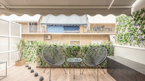 An outdoor patio with two metal chairs and a small table, surrounded by a wooden floor and a decorative wall with climbing plants. - Newly Renovated Loft by Cloudkeys (Athens)