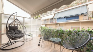 A balcony with wicker chairs, a hanging chair, and potted plants. - Newly Renovated Loft by Cloudkeys (Athens)