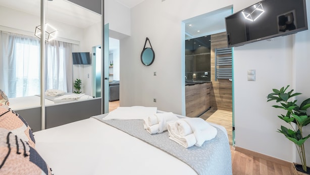 A modern hotel room with a large bed, a mirror, a flat-screen TV, and a view of the bathroom and kitchen. - Newly Renovated Loft by Cloudkeys (Athens)