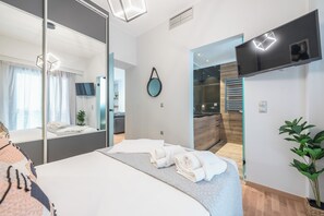 A modern hotel room with a large bed, a mirror, a flat-screen TV, and a view of the bathroom and kitchen. - Newly Renovated Loft by Cloudkeys (Athens)