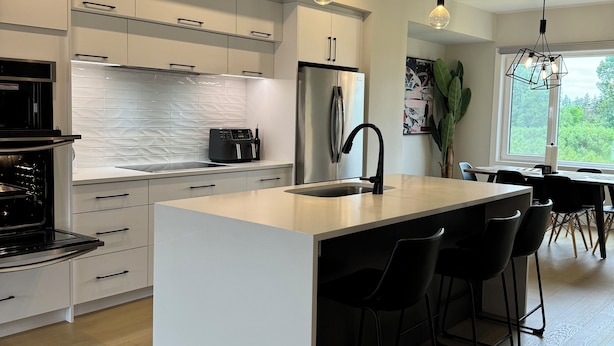 Een moderne keuken met witte kasten, een centraal eiland met barstoelen, een roestvrijstalen koelkast en hanglampen.