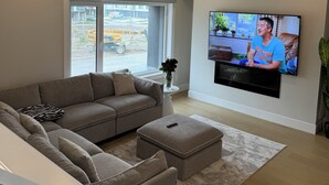 Een moderne woonkamer met een grote flatscreen televisie, een grijze modulaire bank, een klein wit bijzettafeltje en een ronde tafel met een model van de Eiffeltoren.