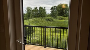 Uitzicht vanaf een balkon met een houten terras en een metalen hekwerk, uitkijkend op een gazon met bomen.