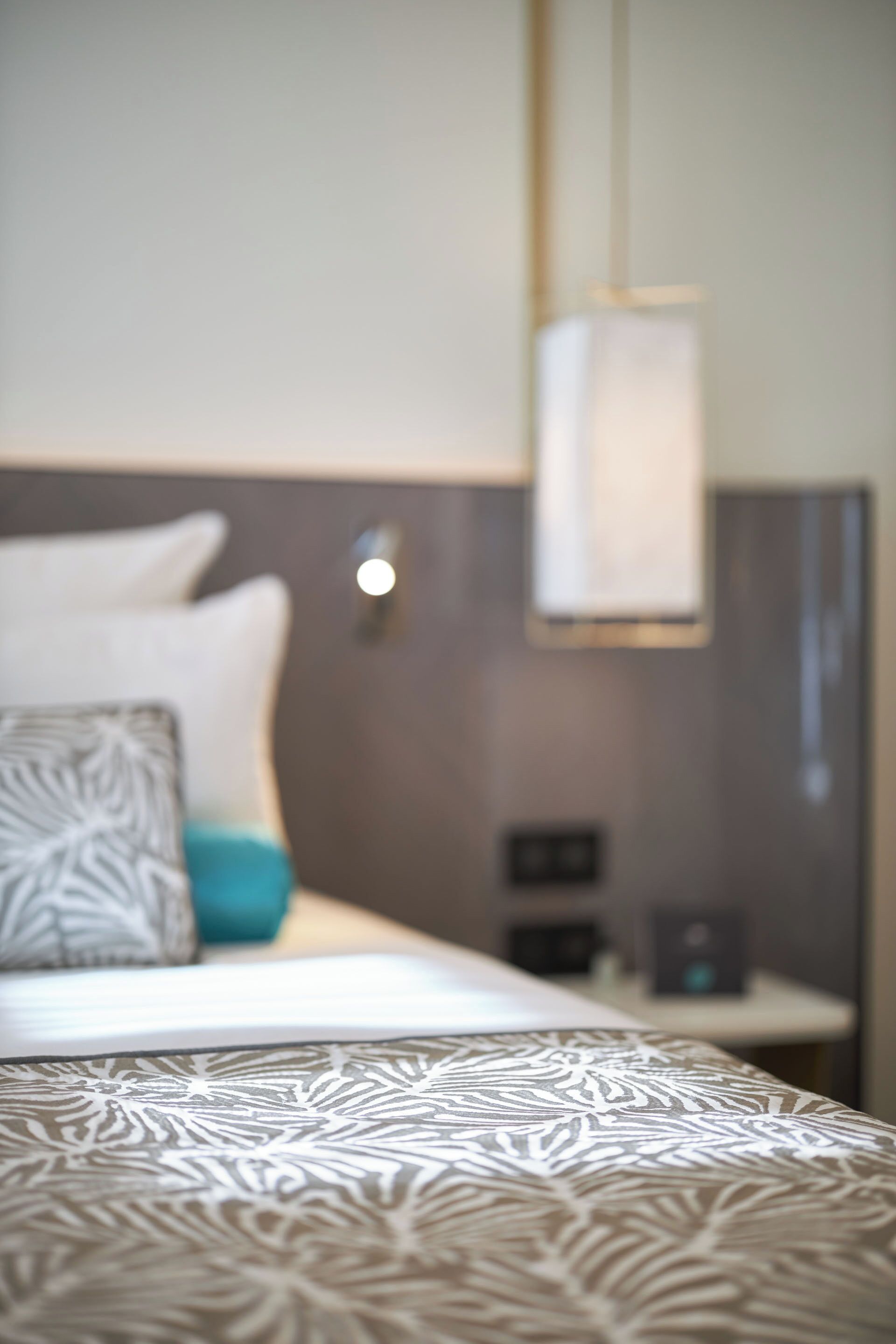 Un lit avec une couvre-lit à motifs, un oreiller à motifs géométriques et une table de chevet avec une lampe.
