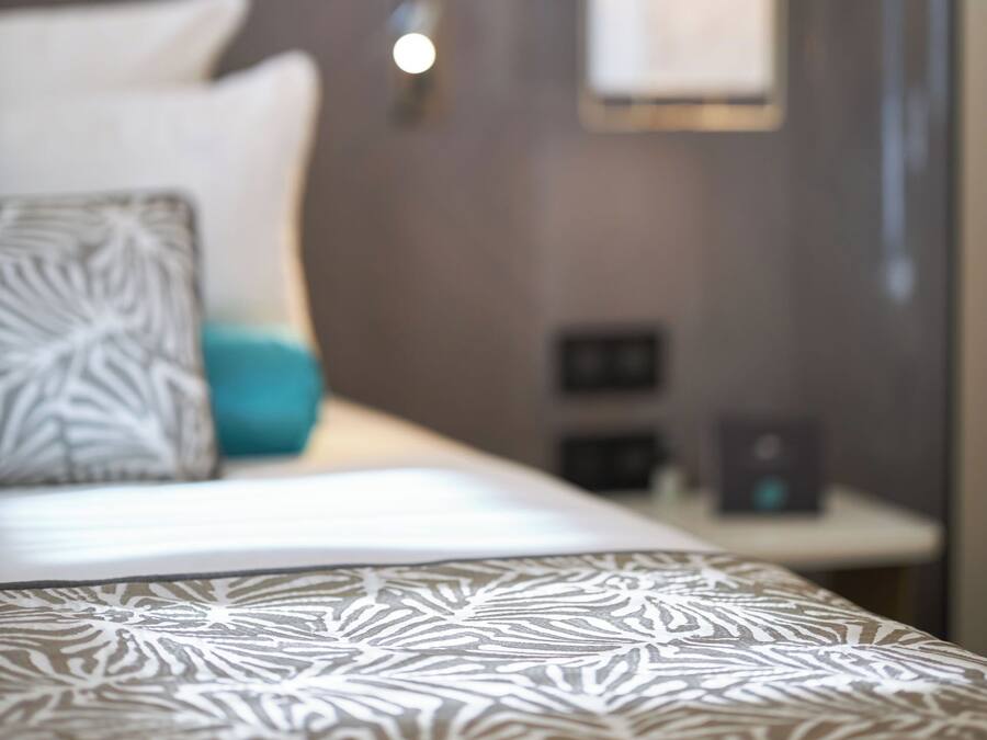 Una cama con una colcha estampada, un almohadón con diseño geométrico y una mesita de noche con una lámpara.