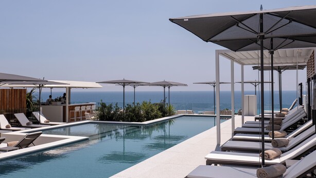 A poolside area with lounge chairs, umbrellas, and a view of the ocean.