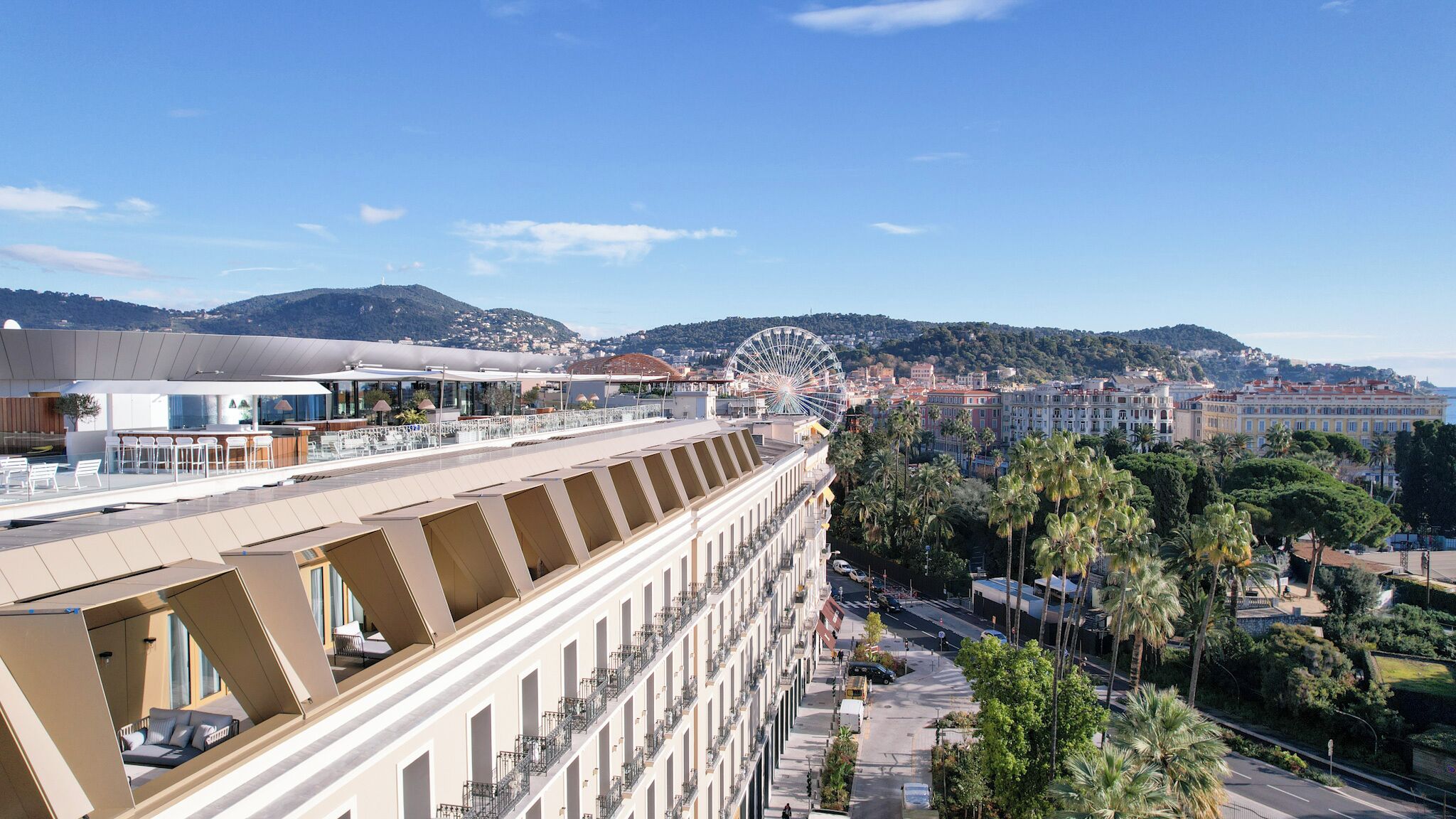 A hotel with a rooftop terrace, a Ferris wheel in the background, and a cityscape with palm trees.