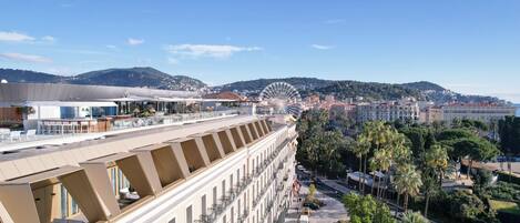 A hotel with a rooftop terrace, a Ferris wheel in the background, and a cityscape with palm trees.