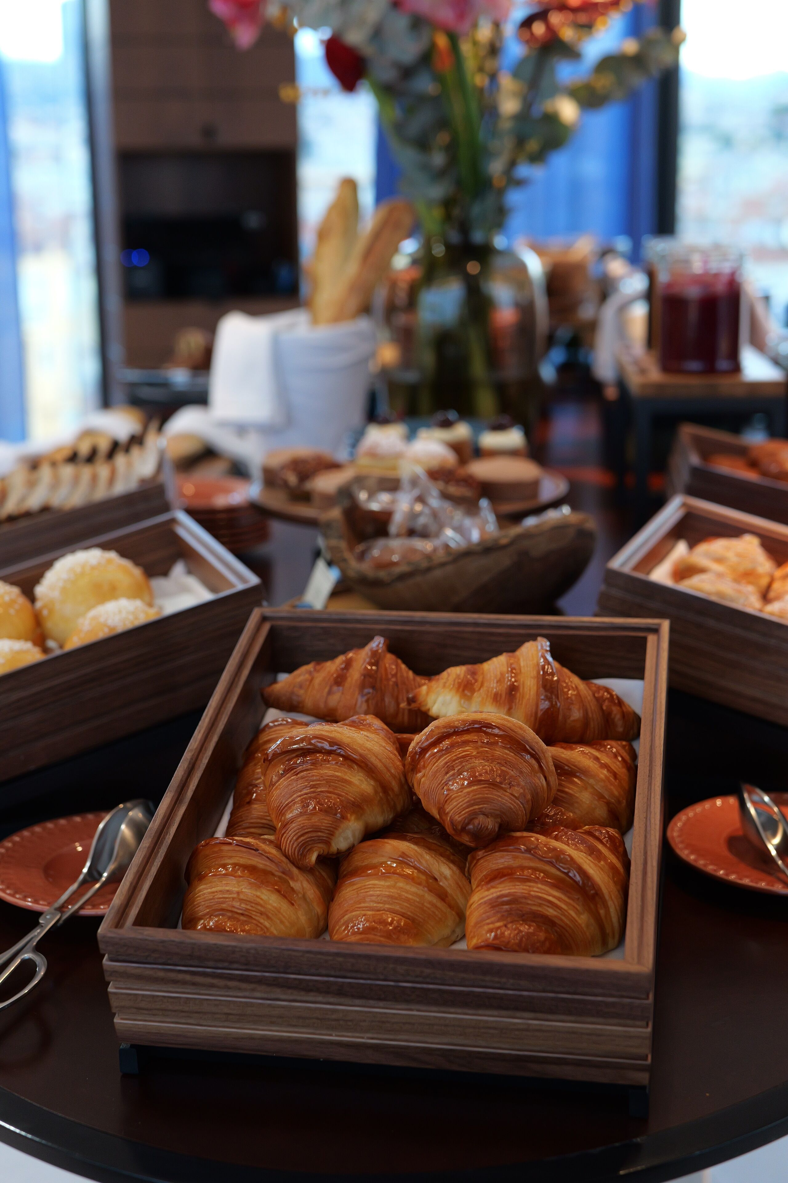 A breakfast buffet with various pastries and bread, including croissants and muffins, arranged on wooden trays.