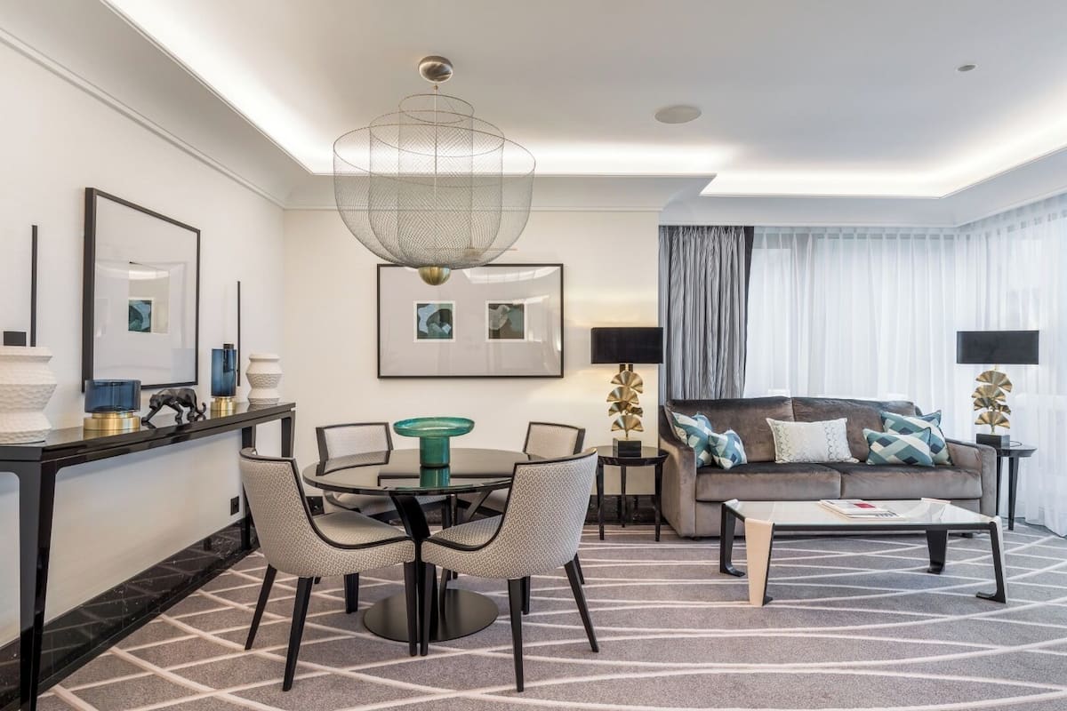 Una habitación de hotel moderna con comedor, un conjunto de sofás y una araña.
