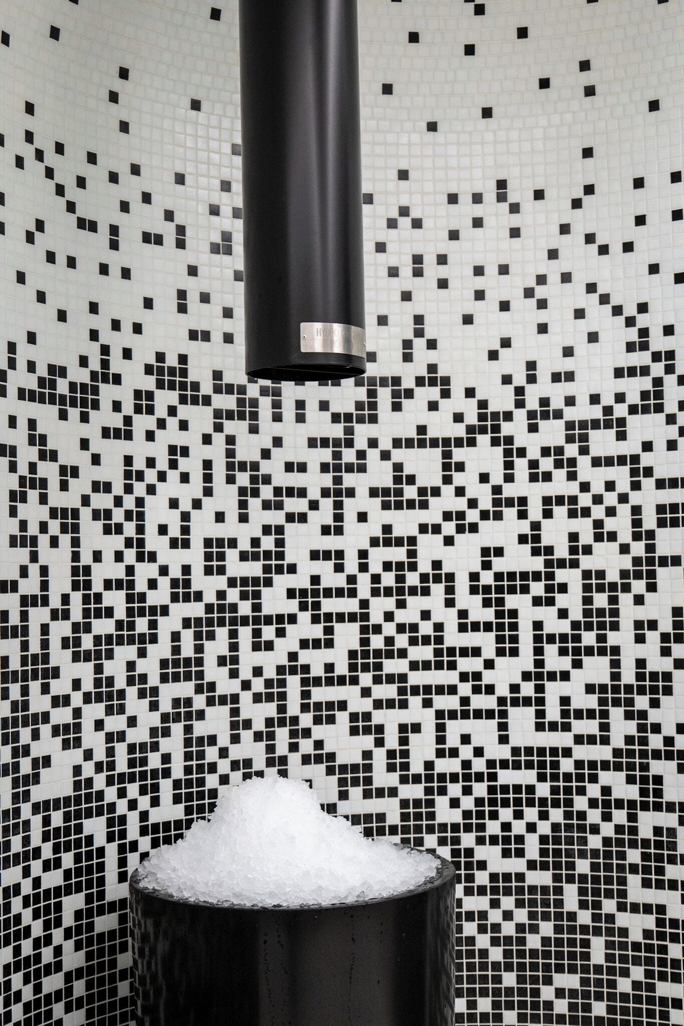 Un recipiente cilíndrico negro lleno de cubos blancos sobre un fondo de baldosas de mosaico blanco y negro.