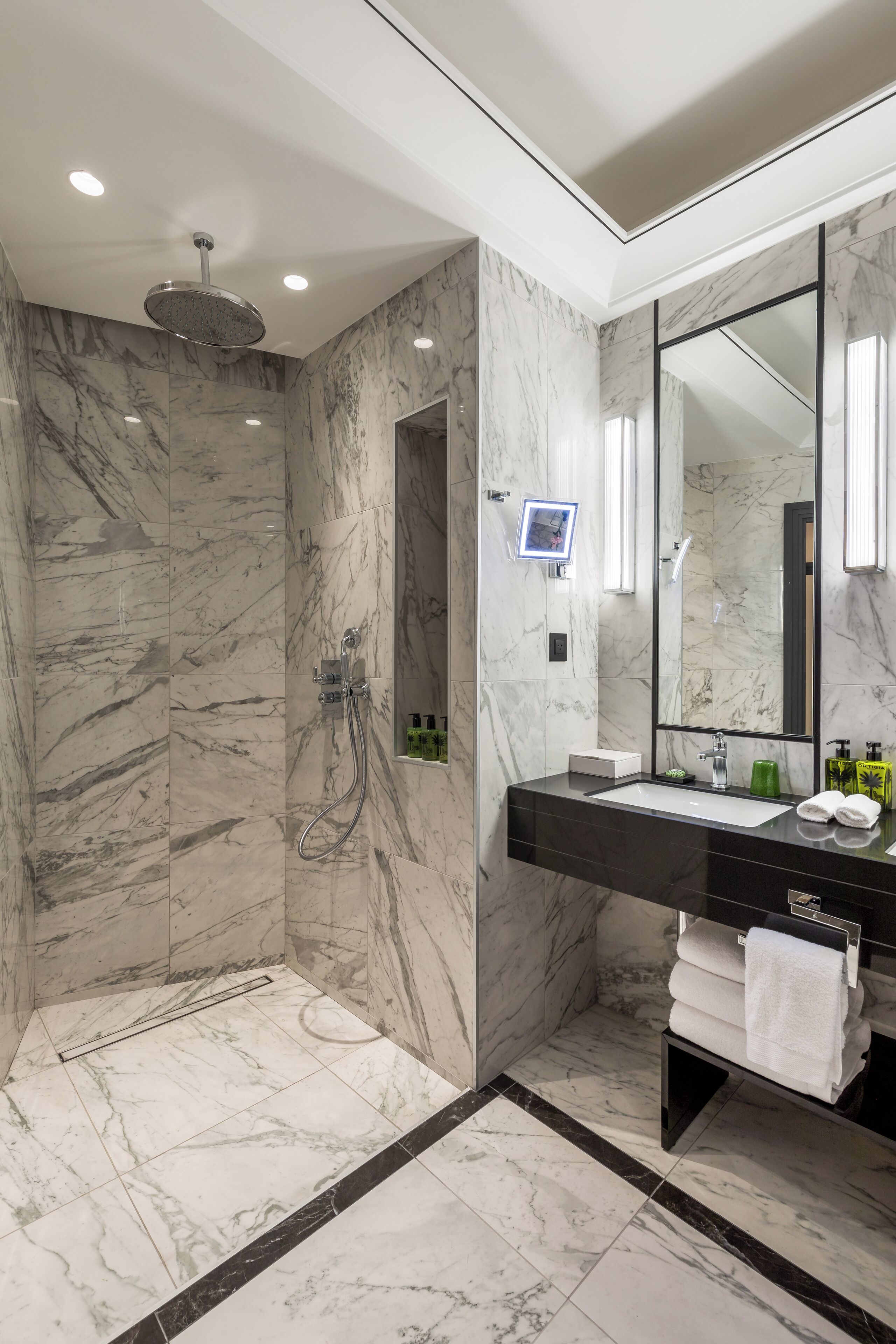 A modern bathroom with a large mirror, marble walls, and a shower area.