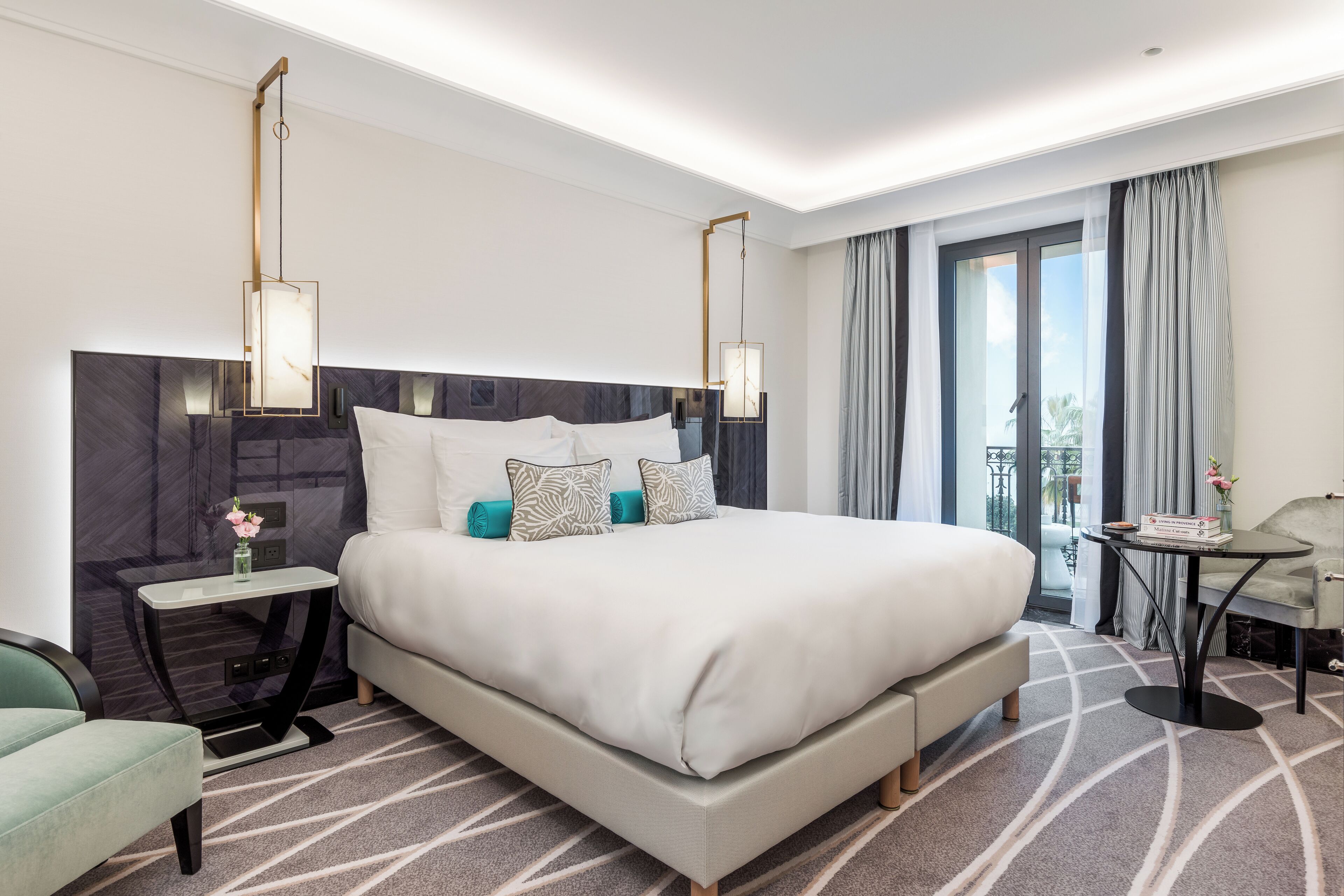 Quarto de hotel moderno com uma cama grande, uma mesinha, uma cadeira e vista para o exterior.