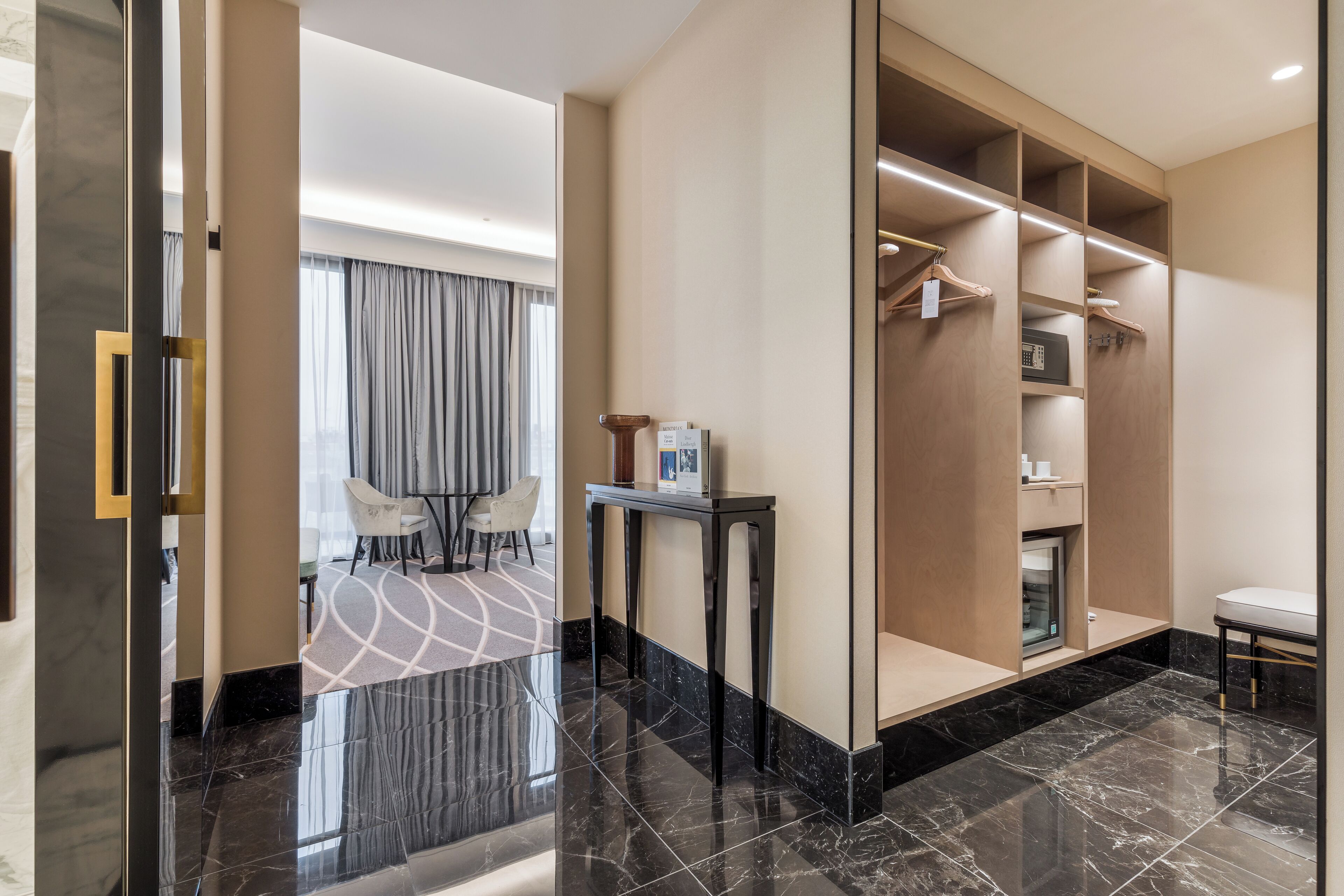 Habitación de hotel con piso de mármol, zona de estar con mesa y sillas, armario con espacio para colgar y una mesita con un marco de fotos.